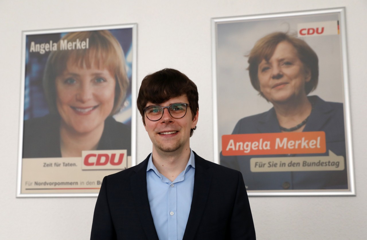 Georg Günther vor älteren Wahlplakaten von Angela Merkel