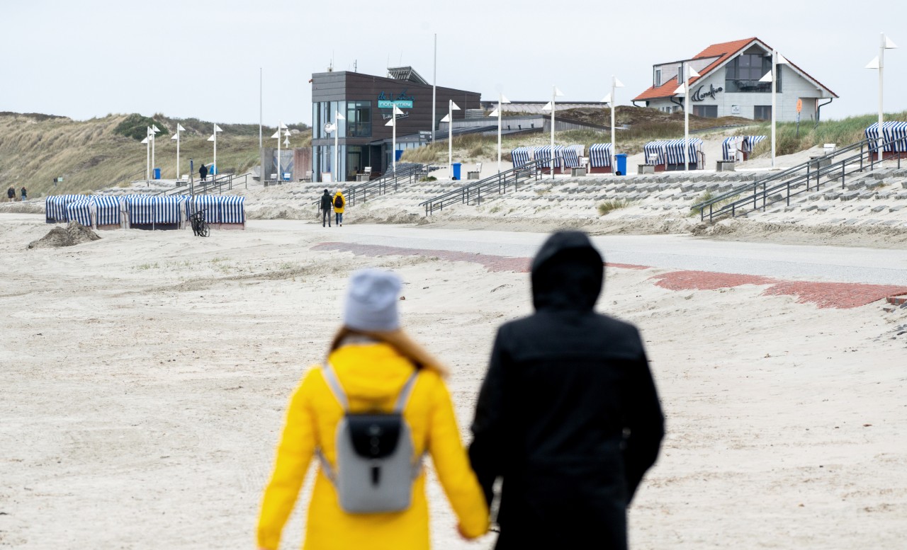 Touristen gehen bei trübem Wetter an der Strandpromenade am Nordstrand von Norderney spazieren. 