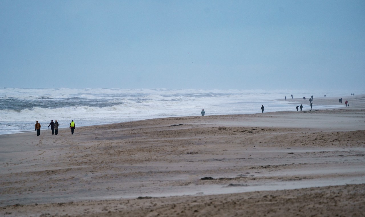 Spaziergänger gehen am Strand von der Nordsee entlang, an dem sich durch starke Sturmböen das Wasser zu hohen Wellen auftürmt.