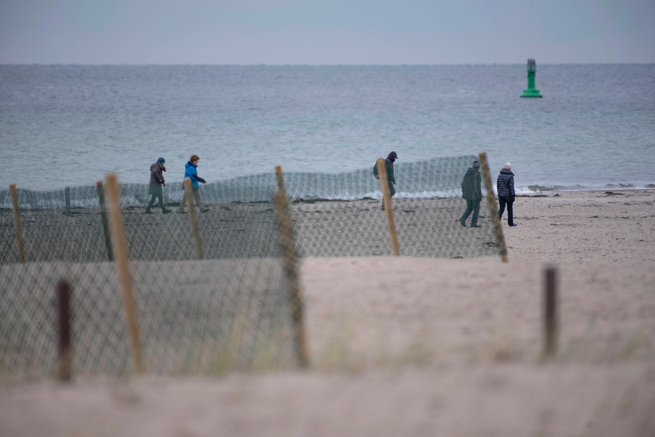 Menschen gehen bei kaltem Wetter an der Ostsee in Warnemünde spazieren. 