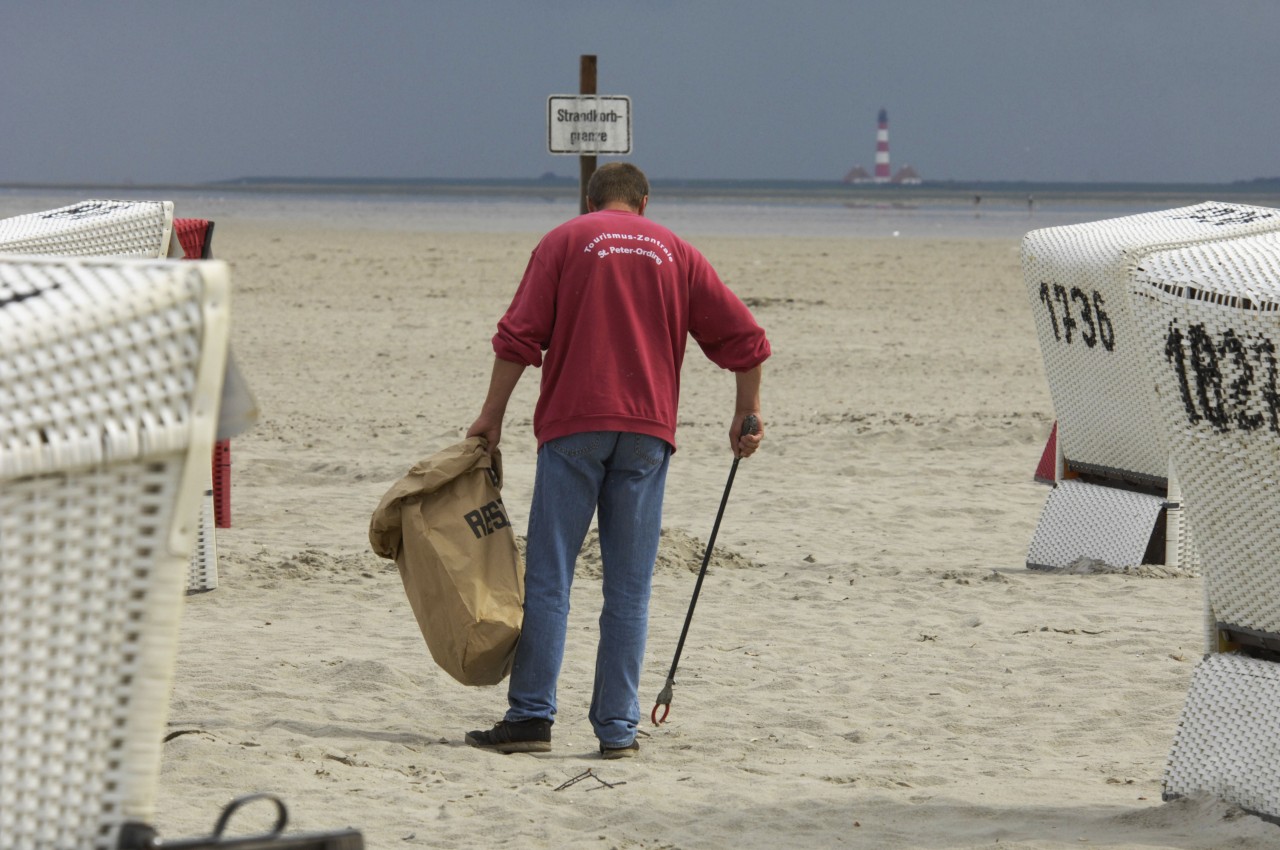 Ein Mitarbeiter der Tourismuszentrale sammelt Müll am Strand von Sankt Peter-Ording auf.