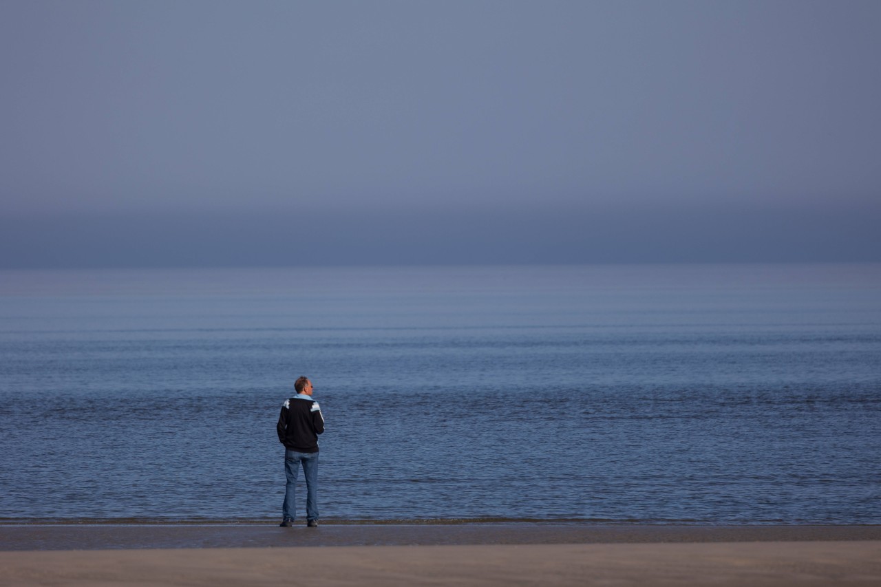 Ein Mann steht am Strand von Sankt Peter-Ording (SPO) und guckt aufs Meer (Symbolfoto).