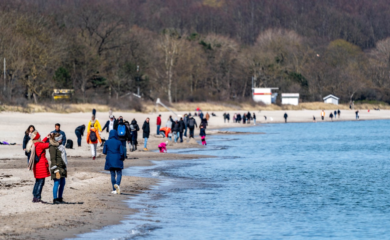 Menschen gehen am Ufer der Ostsee am Timmendorfer Strand entlang.