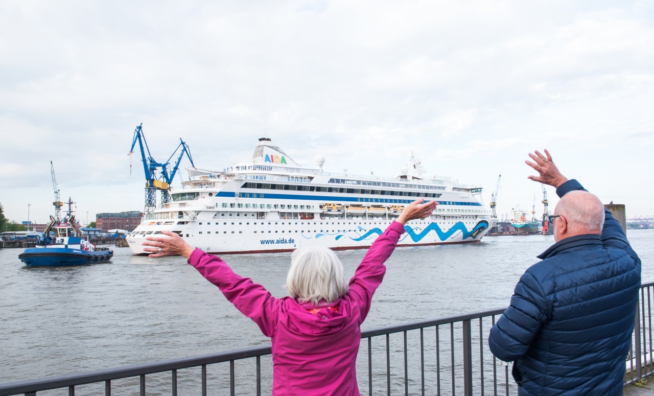 Passanten winken am Morgen zu dem Kreuzfahrtschiff Aida „Aura“, das bei der Werft „Blohm+Voss“ eindockt.