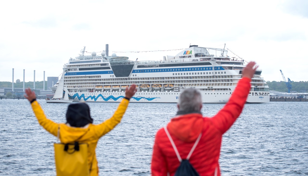 Das Kreuzfahrschiff „Aida sol“ läuft aus dem Hafen aus, während Menschen am Ufer winken.