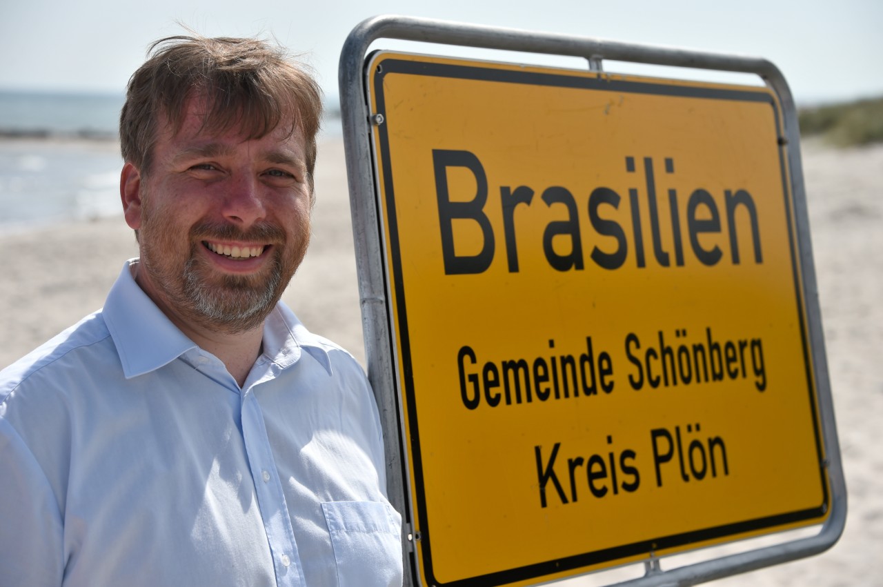 Der ehemalige Bürgermeister der Gemeinde Schönberg Dirk Osbahr steht vor dem Ortsschild „Brasilien“.