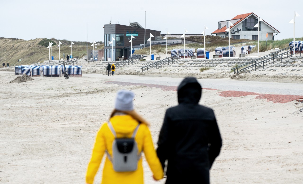 Touristen gehen bei trübem Wetter an der Strandpromenade am Nordstrand von Norderney spazieren.