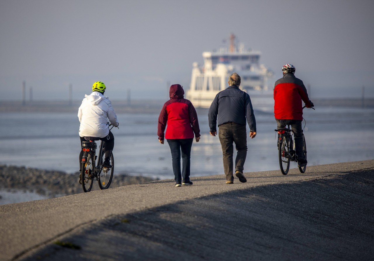 Menschen auf dem Deich von Norderney. Im Hintergrund bahnt sich eine Fähre ihren Weg.
