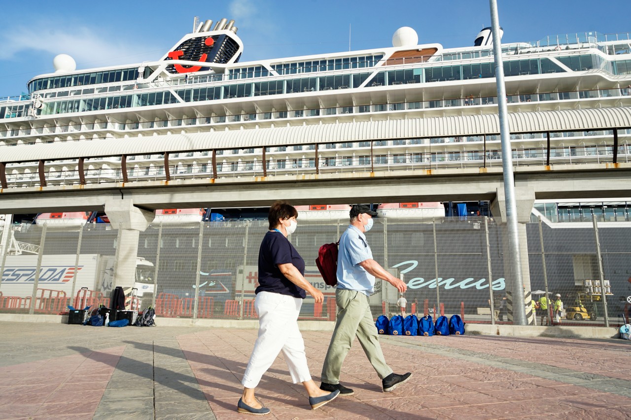 Touristen mit Maske vor einem Dampfer der „Mein Schiff“-Flotte von Tui Cruises.