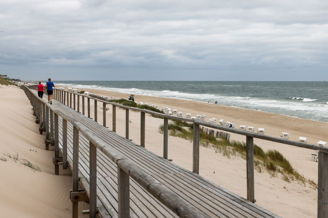 Sylt: Ein Mann und eine Frau joggen bei bewölktem Himmel am Strand von Westerland.