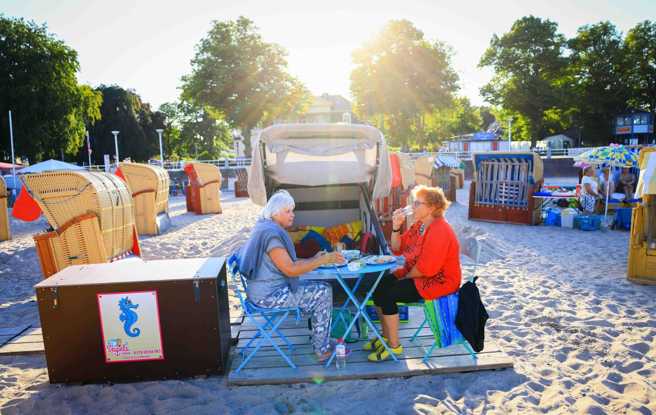 Wiltrud Sadlowski (r) und Marion Schleevoight sitzen im Sonnenuntergang beim Abendbrot vor ihrem gemieteten Schlafstrandkorb an der Ostsee. Das Übernachten am Strand mit Meeresrauschen im Ohr und dem Sternenhimmel im Blick wird immer beliebter.