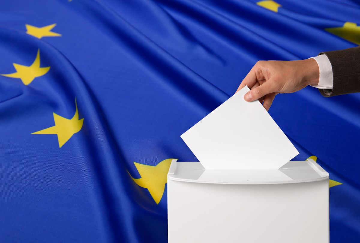 Eine Hand legt einen EU-Wahlzettel in die Wahlurne