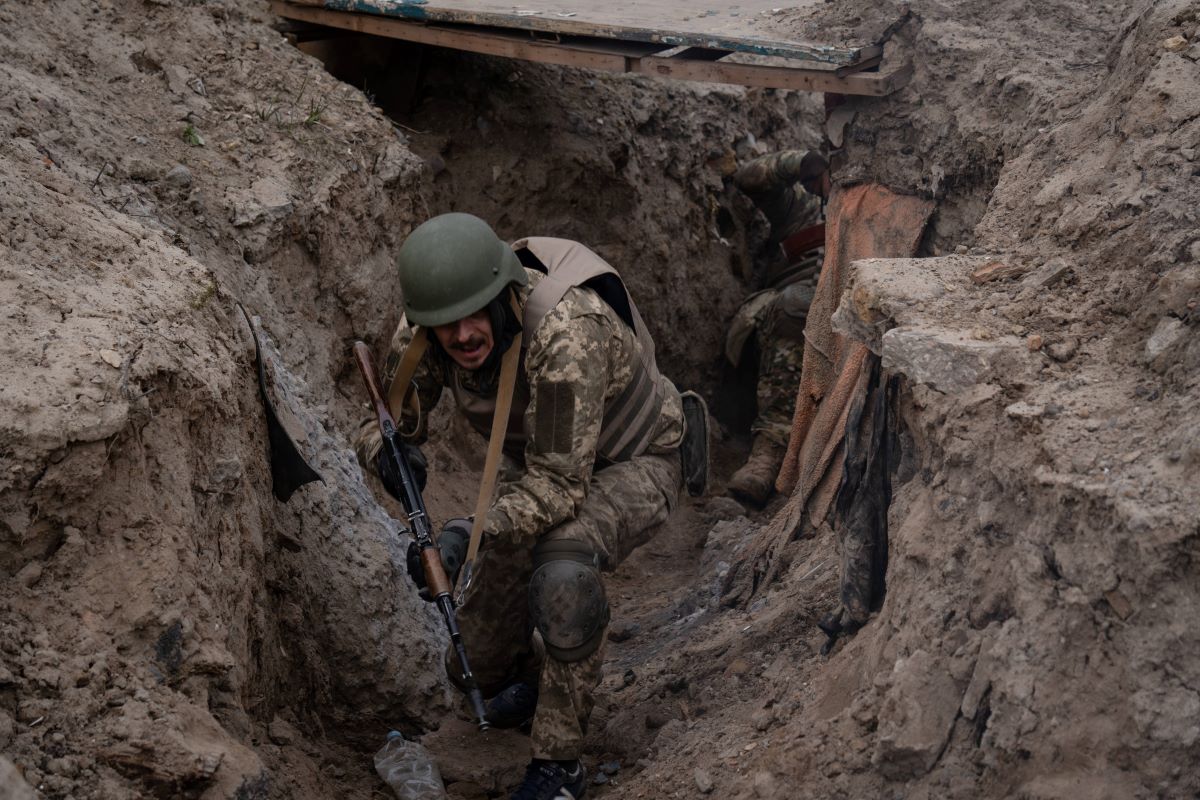 Ein Soldat hockt mit Gewehr im Schützengraben.