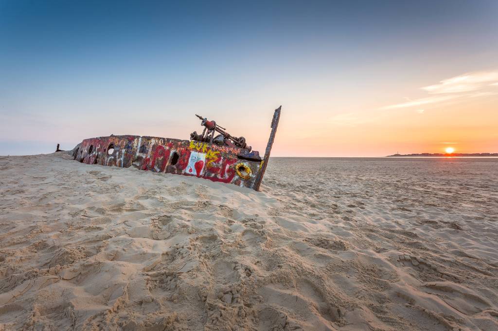 Schiffswrack liegt im Sand bei Sonnenuntergang