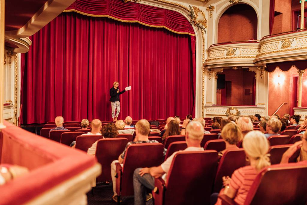 Moderator steht im Theater vor den Vorhängen