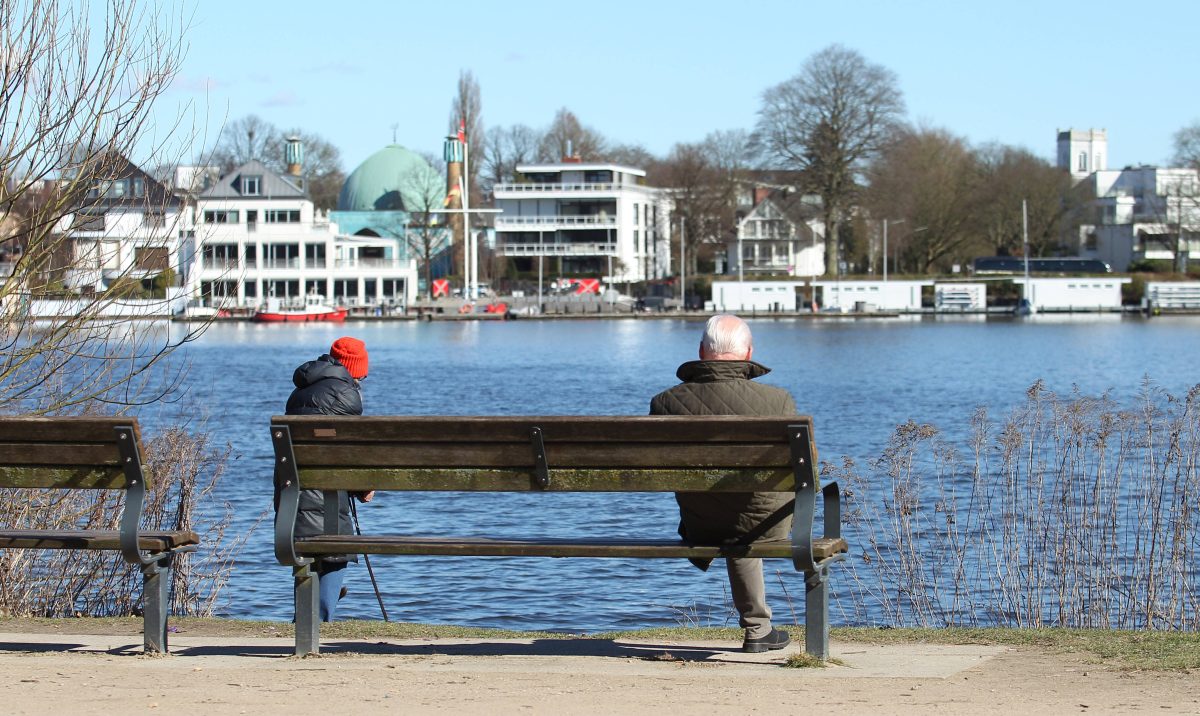 Ein Mann sitzt bei frühlingshaften Temperaturen und Sonnenschein auf einer Sitzbank an der Außenalster, Symbolbild